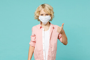 Little kid boy 10s in pink shirt sterile face mask safe from coronavirus virus covid-19 showing thumb up isolated on blue turquoise background children studio portrait. Childhood lifestyle concept.