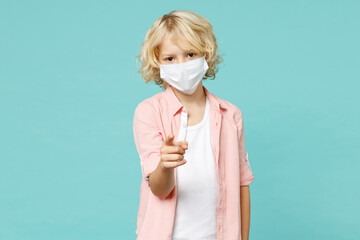 Little kid boy in pink shirt sterile face mask safe from coronavirus virus covid-19 pointing finger on camera on you isolated on blue turquoise background studio portrait. Childhood lifestyle concept.