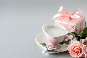 Cup of coffee, pink roses, box with a gift and pink roses on a gray background. Copy space.