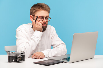 Bored thoughtful man graphic designer holding stylus of graphic tablet in hand and looking at...