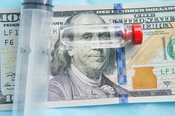 A glass bottle with a clear liquid rests on a hundred dollar bill. The concept of the high cost of...