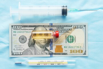 A glass bottle with a clear liquid rests on a dollar bill. The concept of the high cost of the coronavirus vaccine and the high cost of healthcare in the United States.