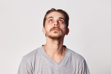 Obraz premium Facet portrait a man looking up. Portrait bristle men in shirt looks up with his head up on a gray background, copy space