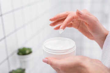 partial view of woman holding jar with face cream