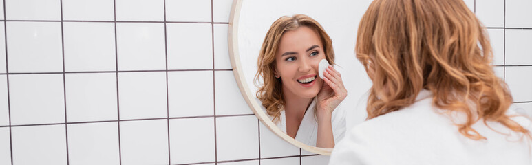 woman applying toner with cotton pad on face and looking at mirror, banner