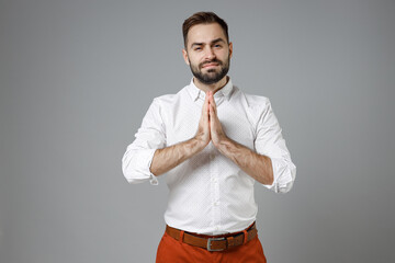 Pleading young bearded business man 20s in white shirt hold hands folded in prayer gesture, begging about something isolated on grey background studio portrait. Achievement career wealth concept.