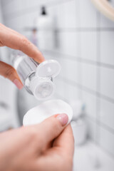 close up of woman holding bottle with toner and cotton pad in bathroom