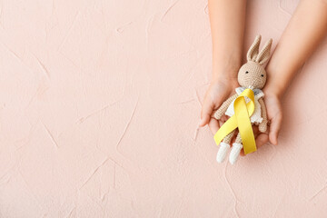 Hands with toy and golden ribbon on color background. Childhood cancer awareness concept