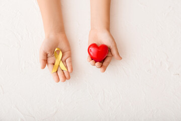 Hands with red heart and golden ribbon on white background. Childhood cancer awareness concept