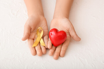 Hands with red heart and golden ribbon on white background. Childhood cancer awareness concept