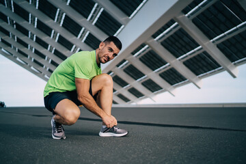 Caucasian sportsman in active clothing and jog shoes tie shoelaces during time for morning running...