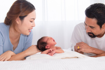 Asian mother and father with beard looking to newborn son crying, parenthood new mom and dad look at infant don't know how to handle baby sickness, newly married couple lie down with baby on bed