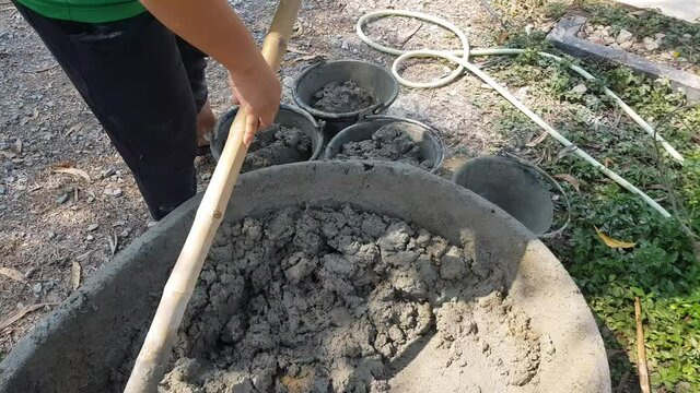 Construction workers pouring cement into buckets for work.