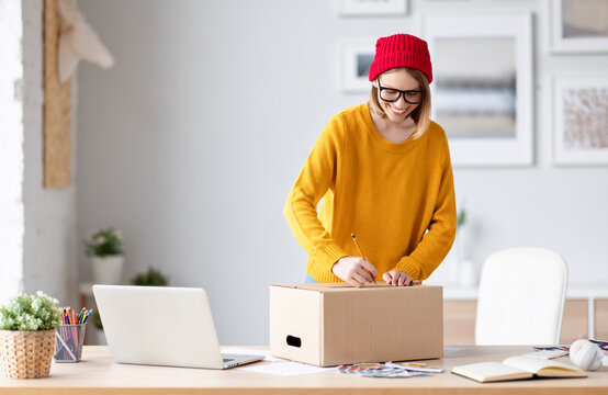 Happy young woman writing address on parcel