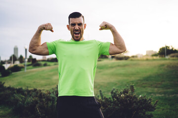 Half length portrait of muscular athletic man showing pumped up arms biceps during cardio training in park, Caucasian bodybuilder feeling confidence and power strength proud of own sportive goals