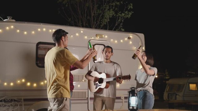 Friends enjoying outdoor guitar party at night, clink and drink beer.