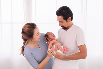 Asian or Hispanic father with beard hold his first child newborn with strong arm, beautiful wife play with baby and try to help husband hold the baby with carefully, happy new married couple with baby