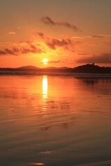 Setting sun silouettes Criccieth Castle and casts beautiful reflections across the rippled sand at Black Rock Beach (potrait).