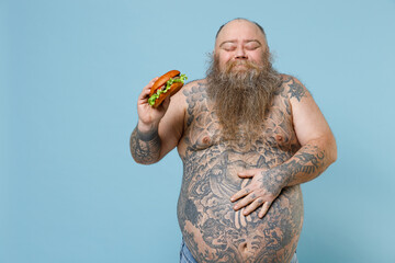 Joyful fat pudge obese chubby overweight man has tattooed naked big belly hold fast food burger put...