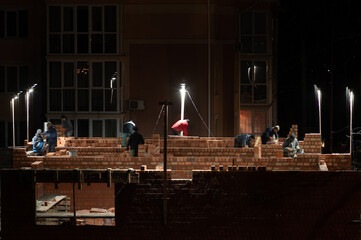 The process of construction of a building of red brick at night under artificial lighting.