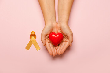 Hands with red heart and golden ribbon on color background. Childhood cancer awareness concept