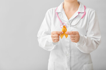 Doctor with golden ribbon on grey background. Childhood cancer awareness concept