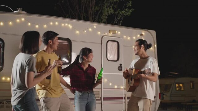 Friends enjoying outdoor guitar party at night, clink and drink beer.