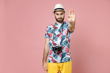 Displeased young traveler tourist man in summer clothes hat with photo camera showing stop gesture with palm isolated on pink background. Passenger traveling on weekends. Air flight journey concept.