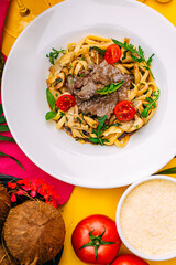 Fetuccini with fried meat and tomatoes on a decorated table