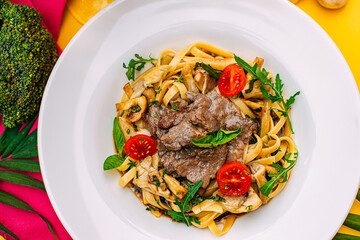 Fetuccini with fried meat and tomatoes on a decorated table