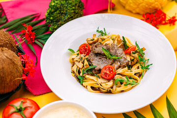 Fetuccini with fried meat and tomatoes on a decorated table