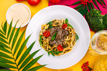 Fetuccini with fried meat and tomatoes on a decorated table