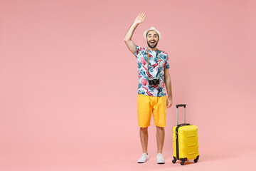 Full length of excited traveler tourist man in summer clothes hat waving greeting with hand as notices someone isolated on pink background. Passenger traveling on weekends. Air flight journey concept.