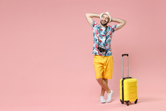 Full length of funny young traveler tourist man in summer clothes hat hold hands behind head isolated on pink background studio portrait. Passenger traveling on weekends. Air flight journey concept.