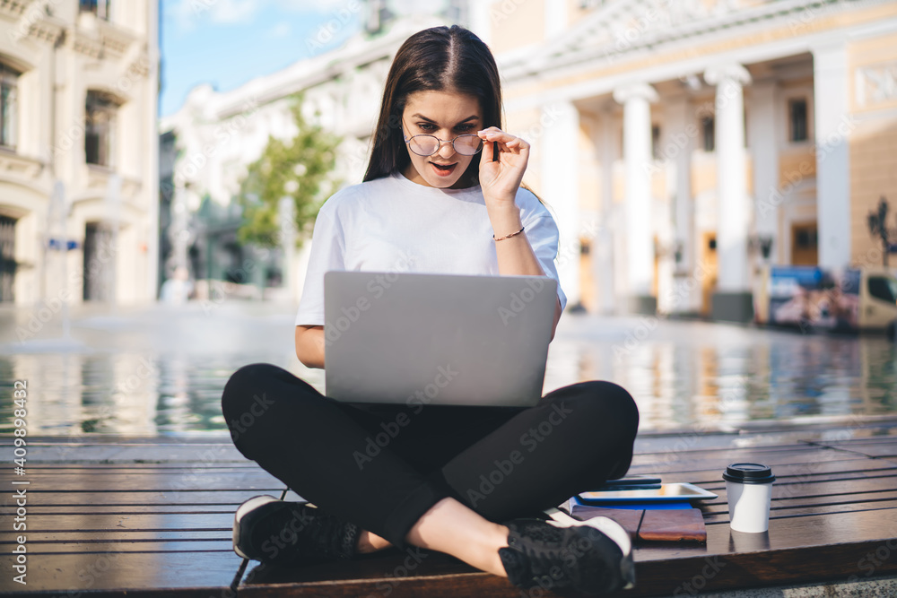Poster amazed hipster girl in optical eyewear shocked with received email message on modern netbook technol