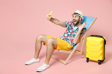 Full length of traveler tourist man in hat sit on deck chair doing selfie shot on mobile phone greeting with hand isolated on pink background. Passenger travel on weekend. Air flight journey concept.