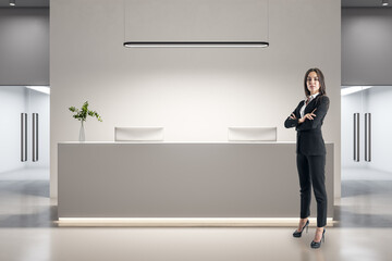 Businesswoman standing in office lobby interior with reception desk.