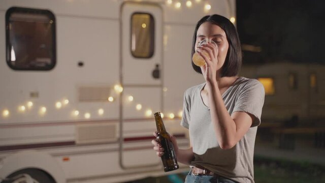 Asian girl holding bottle, drinking glass of beer and smile at night.