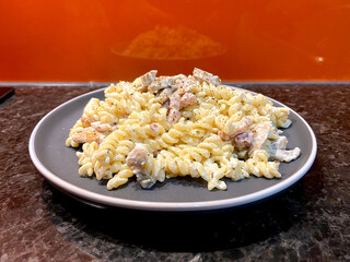 fusilli pasta with white cream sauce with mushrooms and bacon on a gray plate with orange background