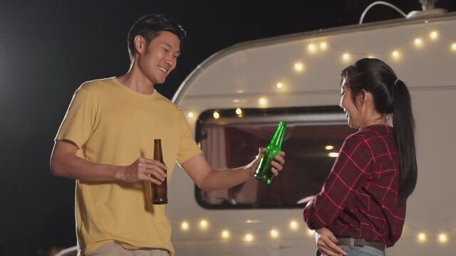 Lovely asian couple clinking, drinking bottles of beer and smiling.
