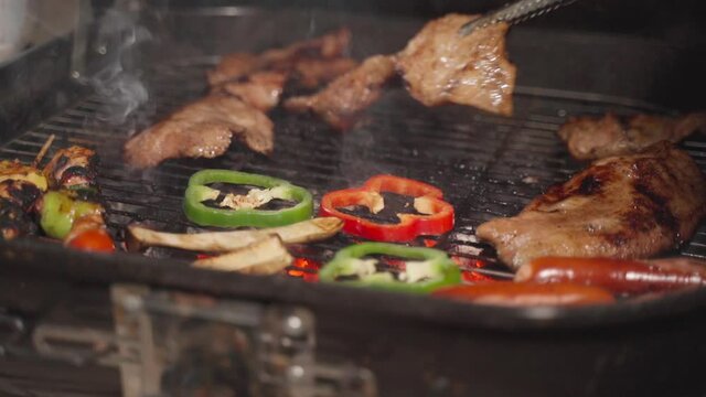 Food tongs holding pork on barbecue grill with smoked from charcoal.