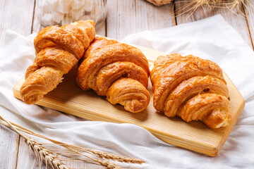 Three french croissants on the wooden cutting board decorated with wheat and napkin
