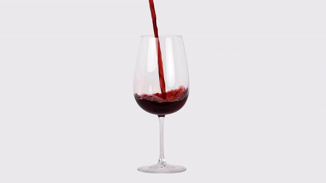 Red wine pouring into wine glass in white studio, close up slow motion