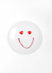 Cute smiley face made of decorative hearts and red ribbon on the plate. Setting the table to celebrate Valentine's Day