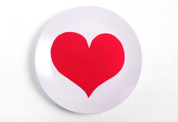 Red cardboard heart on the ceramic plate on the white table. Setting the table to celebrate Valentine's Day