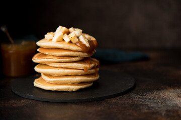American pancakes with caramel and banana on a dark background, selective focus