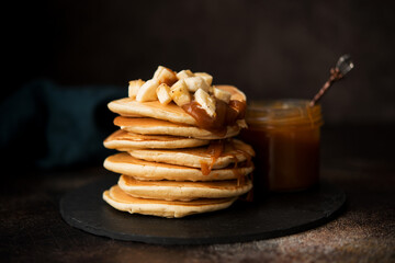 American pancakes with caramel and banana on a dark background, selective focus