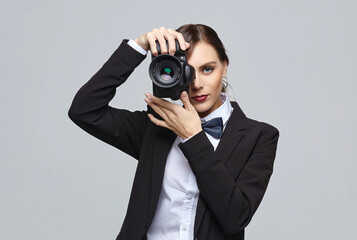 pretty girl photographer in a men's suit and retro hairstyle. posing with the camera in the studio on a white background