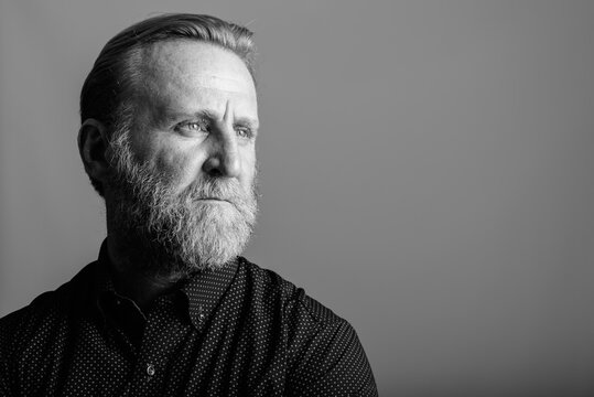 Studio shot of mature bearded man thinking while looking away in gray background
