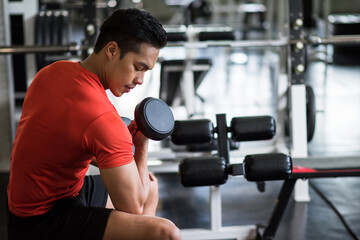 Young fit Asian man exercise dumbbell in gym